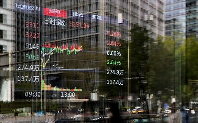 Pedestrians and office buildings are reflected on the window of a brokerage house as an electronic board displays trading data in the Central Business District, in Beijing, China, April 9, 2025. (AP Photo/Andy Wong)