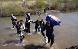 Syrian Alawite families who fled the clashes in Syria hold their luggage as they cross a river marking the border between Syria and northern Lebanon near the village of Heker al-Daher in Akkar province, Lebanon, March 11, 2025. (Hussein Malla/AP)