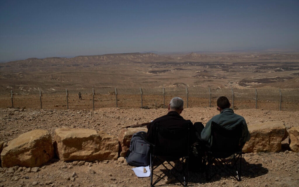 People on the Israeli side of the border with Egypt sit at a lookout overlooking the Sinai desert, while an Egyptian soldier stands near on the other side of the border, as seen from a road that was opened for two days during the Jewish holiday of Passover, April 16, 2025. (AP Photo/Leo Correa)