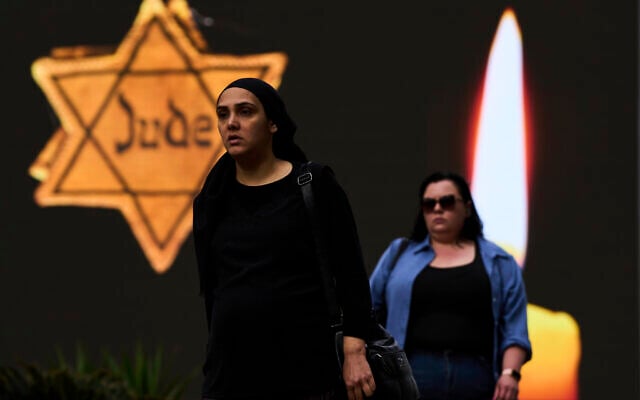 People walk next to a billboard showing a yellow Star of David that reads "Jude," Jew in German, resembling the one Jews were forced to wear in Nazi Germany, during the annual Holocaust Remembrance Day in Ramat Gan, April 24, 2025. (AP Photo/Oded Balilty)