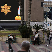 People walk next to a billboard showing a yellow Star of David that reads "Jude," Jew in German, resembling the one Jews were forced to wear in Nazi Germany, during the annual Holocaust Remembrance Day in Ramat Gan, April 24, 2025. (AP Photo/Oded Balilty)