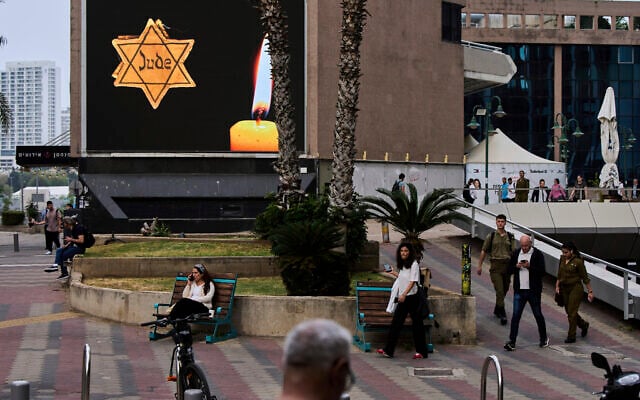People walk next to a billboard showing a yellow Star of David that reads "Jude," Jew in German, resembling the one Jews were forced to wear in Nazi Germany, during the annual Holocaust Remembrance Day in Ramat Gan, April 24, 2025. (AP Photo/Oded Balilty)