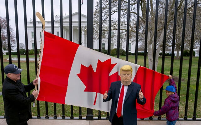 Toronto residents Douglas Bloomfield, left, and his son Phoenix, right, hold a Canadian flag and an ice hockey stick to show their support for Canada regarding trade tariffs as they pose with with another visitor to the city wearing a mask of US President Donald Trump, in front of the White House in Washington, March 13, 2025. (AP Photo/Ben Curtis)