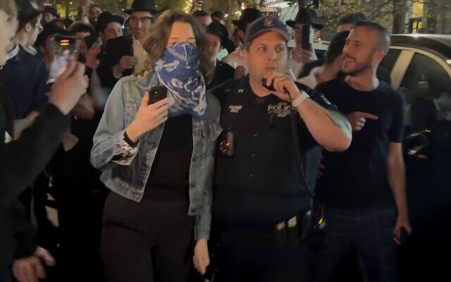 This image taken from video shows a woman and a police officer as they are pursued by a group of Orthodox Jewish men in the Crown Heights section of Brooklyn, New York, following an anti-Israel protest outside a synagogue on April 24, 2025. (AP Photo)