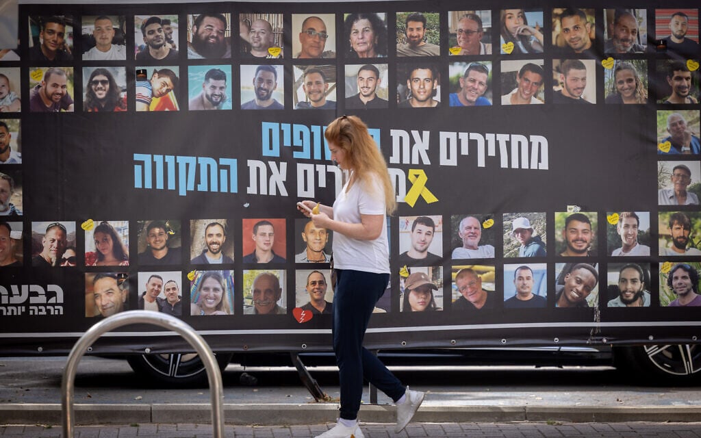 A woman walks past a poster depicting hostages held in Gaza, in Tel Aviv on April 6, 2025. (Miriam Alster/FLASH90)