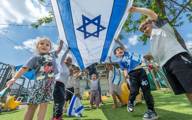 Illustrative: Children play with Israeli flags ahead of Israel's 77th Independence Day at a kindergarten in Moshav Yashresh in central Israel, April 29, 2025. (Yossi Aloni/Flash90)