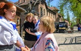 Holocaust survivor Irene Shashar (R) speaks to rescued hostage Ori Megidish (L), while Holocaust survivor Gita Kaufman and released hostage Agam Berger embrace, draped in an Israeli flag outside the "Arbeit Macht Frei" sign at Auschwitz during March of the Living on April 24, 2025 in Oswiecim, Poland. (Alexi Rosenfeld/Getty Images, via JTA)