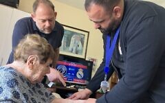 Dr. Fadi Badarna, right, a volunteer eye doctor with LeMa’anam (“for their sake” in Hebrew), a nonprofit organization providing free home healthcare to Holocaust survivors, and Aviv Paz, a LeMa'anam employee, look at the number tattoo that Chana Sandouvsky received in Auschwitz, in her home in Kiryat Bialik on April 16, 2025. (Diana Bletter/Times of Israel)