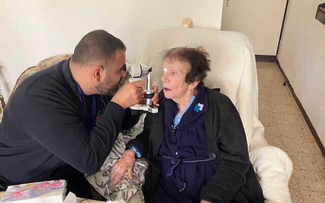 Dr. Fadi Badarna, left, a volunteer eye doctor with LeMa’anam (“for their sake” in Hebrew), a non-profit organization providing timely healthcare free of charge to Holocaust survivors in their homes, examines the eyes of Henia Hirsh in her home in Kiryat Ysm on April 16, 2025. (Diana Bletter/Times of Israel)