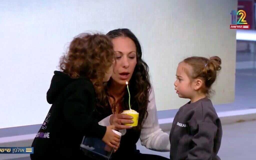 Lishay Miran Lavi blows out a candle on a birthday cupcake for her hostage husband Omri, along with her two daughers Roni and Alma at Channel 12's studio on April 11, 2025. (Screen capture/Channel 12)