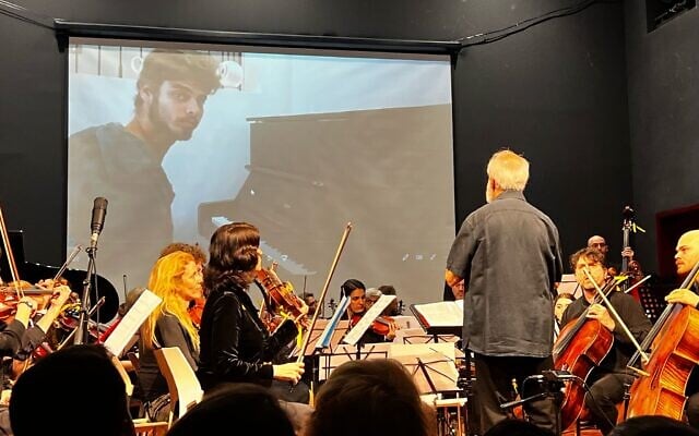 The Lu Yehi Orchestra accompanies a video of Alon Ohel playing piano, before he was taken captive, in Jerusalem on April 8, 2025 (Courtesy)