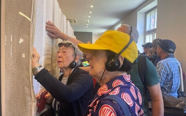 Holocaust survivor Suzanne Rosenberg, far left, looks in the Book of Names at Block 27 at Auschwitz to find her uncle's name on April 23, 2025 (Jessica Steinberg/Times of Israel)