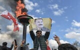 A man holds a portrait of Abdullah Ocalan, Turkish-jailed founder of the Kurdistan Workers' Party (PKK), next to a bonfire during a gathering for Nowruz celebrations marking the New Year of the Persian calendar and the first day of spring, in Diyarbakir, southeastern Turkey, on March 21, 2025. (Ilyas AKENGIN / AFP)