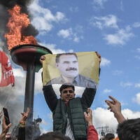 A man holds a portrait of Abdullah Ocalan, Turkish-jailed founder of the Kurdistan Workers' Party (PKK), next to a bonfire during a gathering for Nowruz celebrations marking the New Year of the Persian calendar and the first day of spring, in Diyarbakir, southeastern Turkey, on March 21, 2025. (Ilyas AKENGIN / AFP)