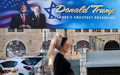People walk next to a sign with portraits of US President Donald Trump (L) and US Ambassador to Israel Mike Huckabee in central Jerusalem on May 7, 2025. (Ahmad Gharabli/AFP)