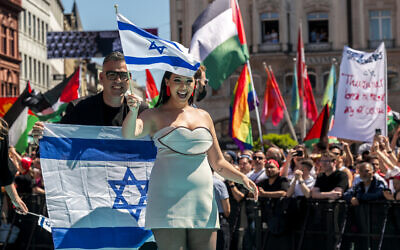 Israeli singer Yuval Raphael, representing Israel with the song, 'New Day Will Rise,' walks on the turquoise carpet next to the Basel Town Hall, with protesters' Palestinian flags behind, during the opening ceremony of the Eurovision Song Contest 2025  in Basel, Switzerland, on May 11, 2025. (Fabrice COFFRINI / AFP)