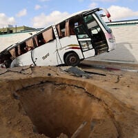 A man walks past a bus inside a crater in the aftermath of an Israeli strike in Khan Younis in the southern Gaza Strip on May 14, 2025.  (Photo by Eyad BABA / AFP)