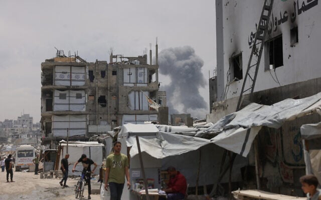 Palestinians walk past the damaged Kamal Adwan medical facility (R) while smoke billows in the background during Israeli bombardment east of Jabaliya in the northern Gaza Strip on May 15, 2025. (Bashar Taleb/AFP)