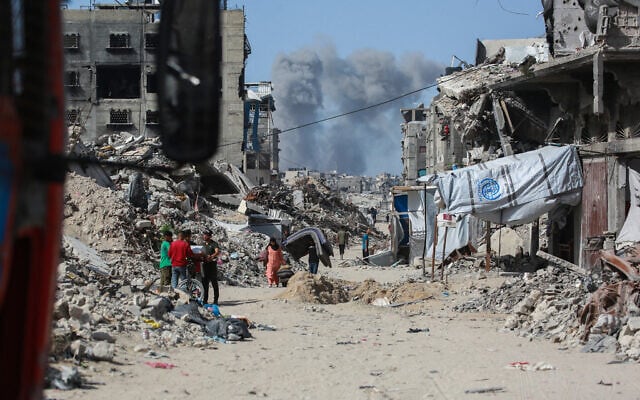 Smoke billows to the north as Palestinians move with their belogings through Jabalia while fleeing the northern Gaza Strip towards Gaza City on May 19, 2025, amid Israeli evacuation orders and ongoing strikes. (Bashar TALEB / AFP)