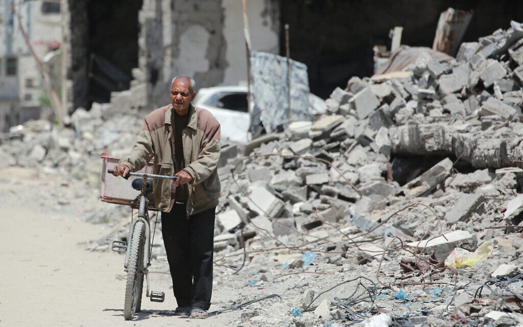 An elderly Palestinian man pushes a bicycle past the rubble of destroyed buildings, in Gaza City, on May 20, 2025. (Bashar TALEB / AFP)
