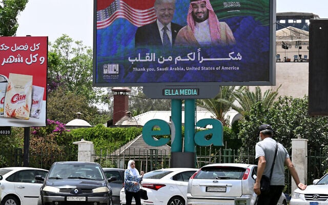 People walk past a billboard displaying portraits of Saudi Crown Prince Mohammed bin Salman and US President Donald Trump with a slogan thanking Saudi Arabia and the United States, in Damascus on May 14, 2025 (LOUAI BESHARA / AFP)