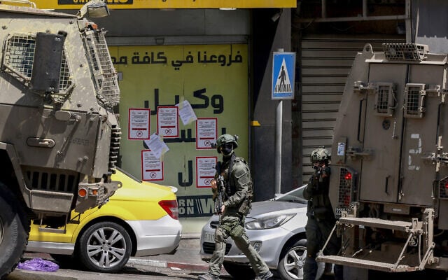 Israeli troops storm a currency exchange shop next to signs warning people not to deal with the Gulf exchange company in Hebron in the southern West Bank on May 27, 2025. (HAZEM BADER / AFP)