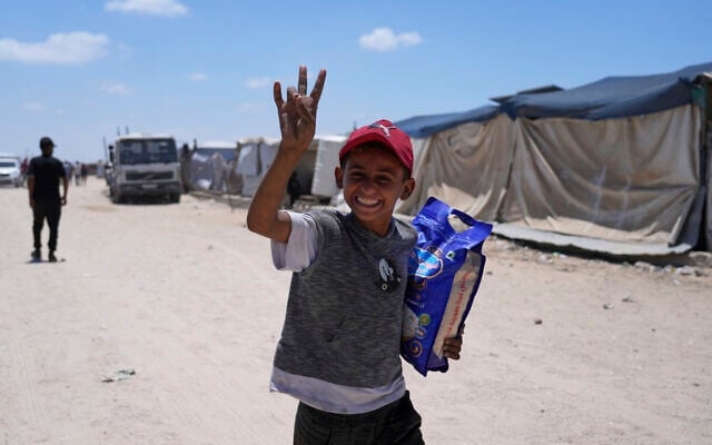 A Palestinian child smiles to the camera as carries a bag of rice delivered by the US-backed Gaza Humanitarian Foundation, after receiving the supplies in Rafah, as he arrive in Khan Younis, southern Gaza Strip, on May 28, 2025. (AP Photo/Abdel Kareem Hana)