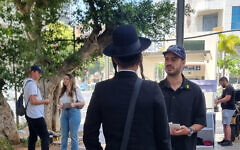 Hozrim Betvuna founder Naor Narkis, right, speaks with a passerby in the largely ultra-Orthodox central Israeli city of Bnei Brak, May 2025. (Alexandra Vardi)