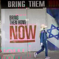 A woman walks by a poster calling for the release of the hostages, in Tel Aviv, on May 18, 2025 (Miriam Alster/Flash90)