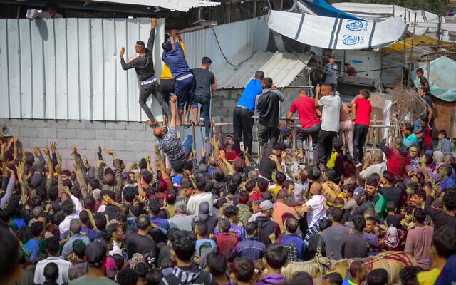 Displaced Palestinians reach out for bread being distributed through a bakery window in Nuseirat Refugee Camp, in the central Gaza Strip, May 22, 2025. (Ali Hassan/Flash90)