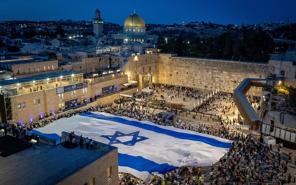 People hold a giant Israel flag at the Western Wall in Jerusalem's Old City, on the eve of Jerusalem Day, May 25, 2025. (Chaim Goldberg/Flash90)
