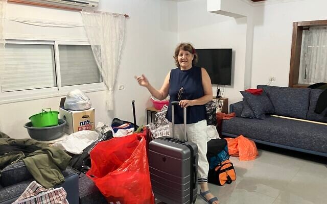Shula Giladi stands with her suitcase and belongings in her house in Shtula, damaged by Hezbollah attacks during the Israel-Hezbollah war on May 23, 2025. (Diana Bletter/Times of Israel)