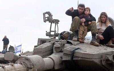 An Israeli soldier, his wife and their child sitting on a tank, during a family visit upon his return from a mission in the Gaza Strip on January 28, 2024. (Menahem KAHANA / AFP)