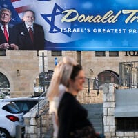 People walk next to a sign with portraits of US President Donald Trump (L) and US Ambassador to Israel Mike Huckabee in central Jerusalem on May 7, 2025. (Ahmad Gharabli/AFP)