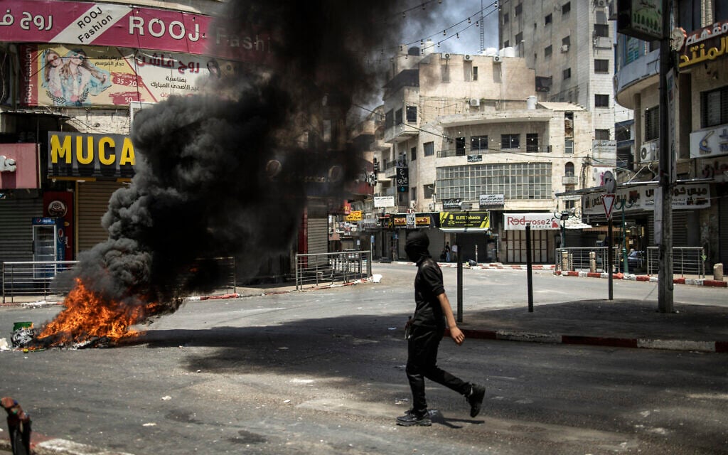 A masked Palestinian youth walks past flaming tyres set up to block a road during a large-scale Israeli military raid in the old town of Nablus in the West Bank on June 10, 2025. (Photo by JOHN WESSELS / AFP) A masked Palestinian youth walks past flaming tyres set up to block a road during a large-scale Israeli military raid in the old town of Nablus in the West Bank on June 10, 2025. (Photo by JOHN WESSELS / AFP)
