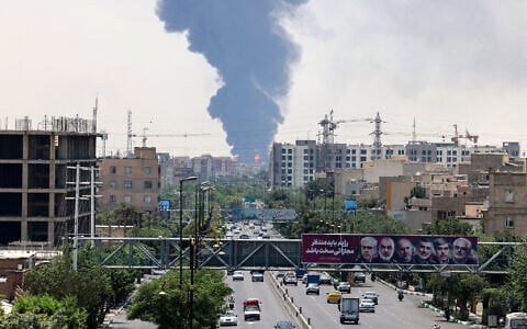 Portraits of Iranian military generals and nuclear scientists, killed in Israel's June 13 attack are displayed above a road, as a plume of heavy smoke and fire rise from an oil refinery in southern Tehran, after it was hit in an overnight Israeli strike, on June 15, 2025. (ATTA KENARE / AFP)