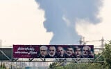 Portraits of Iranian military generals and nuclear scientists, killed in Israel's June 13 attack are displayed above a road, as a plume of heavy smoke rises from an oil refinery in southern Tehran, after it was hit in an overnight Israeli strike, on June 15, 2025. (ATTA KENARE / AFP)