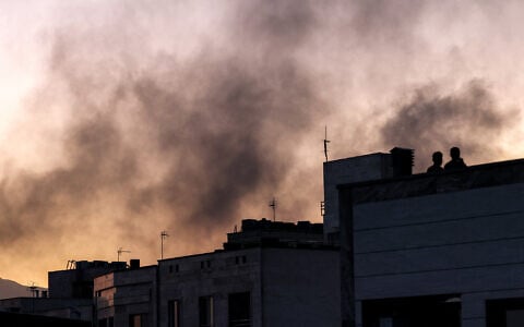 People stand on a rooftop as smoke billows following an Israeli strike in Tehran on June 17, 2025. (Atta Kenare/AFP)