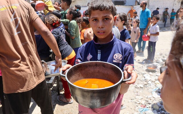 A Palestinian boy carries a pot with food collected at a charity kitchen providing hot meals in Rimal neighbourhood in Gaza City on June 18, 2025. (Omar AL-QATTAA / AFP)