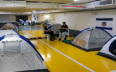 People sit outside pitched tents as they take shelter at an underground parking garage amid fears of an Iranian missile attack, in central Tel Aviv, June 18, 2025. (Ahmad Gharabli/AFP)