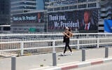 A woman walks on a bridge in front of banners bearing a pictures of US President Donald Trump accompanied by a messages, in Tel Aviv on June 22, 2025 (AHMAD GHARABLI / AFP)