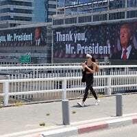 A woman walks on a bridge in front of banners bearing a pictures of US President Donald Trump accompanied by a messages, in Tel Aviv on June 22, 2025 (AHMAD GHARABLI / AFP)
