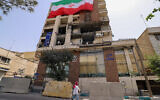 A woman walks past a residential building that was hit in an Israeli strike covered with a big Iranian flag, in Tehran on June 25, 2025. (ATTA KENARE / AFP)
