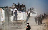 Armed Palestinians sit on trucks carrying humanitarian aid near the Zikim border crossing between Israel and Beit Lahia in the northern Gaza Strip, June 25, 2025. (Ali Qariqa/Flash90)