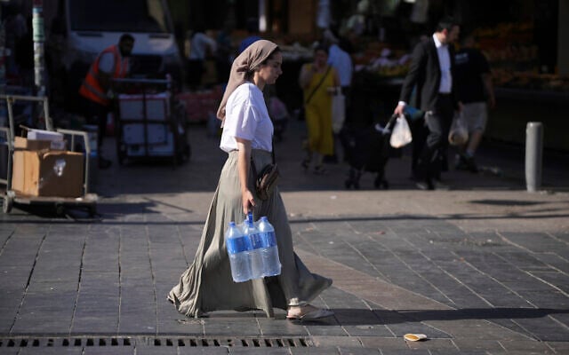 A woman carries water at the Mahane Yehuda market in Jerusalem ahead of Shabbat, June 13, 2025. (AP Photo/Ohad Zwigenberg) A woman carries water at the Mahane Yehuda market in Jerusalem ahead of Shabbat, June 13, 2025. (AP Photo/Ohad Zwigenberg)