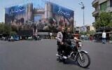 Illustrative: A man flashes a victory sign while riding his motorbike past an anti-Israeli banner depicting Iranian soldiers heading to attack Israeli territory, at Islamic Revolution Square in Tehran, Iran, June 14, 2025. (AP Photo/Vahid Salemi)