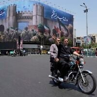 Illustrative: A man flashes a victory sign while riding his motorbike past an anti-Israeli banner depicting Iranian soldiers heading to attack Israeli territory, at Islamic Revolution Square in Tehran, Iran, June 14, 2025. (AP Photo/Vahid Salemi)