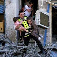 A rescue worker evacuates two children from the site where a missile launched from Iran struck in Haifa, Israel, Sunday, June 22, 2025. (AP Photo/Baz Ratner)