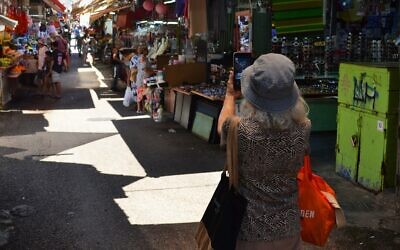 A woman stops to take a picture of Carmel Market in Tel Aviv, a day after the announcement of a ceasefire between Israel and Iran, June 25, 2025. (Stav Levaton/Times of Israel)