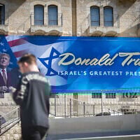 People walk next to a sign with a portrait of US President Donald Trump in central Jerusalem, May 7, 2025. (Yonatan Sindel/Flash90)